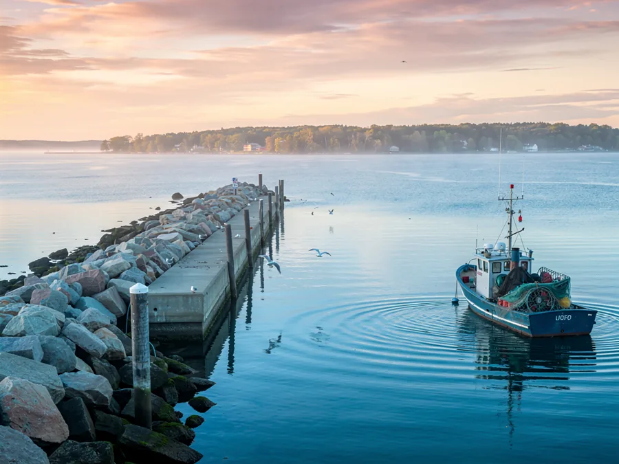 A Great Lakes harbour at sunrise, a stone breakwater running out into open water and a fishing boat coming in