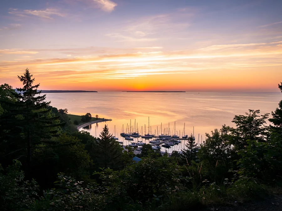 A wide freshwater bay at sunset seen from a wooded bluff, a small harbour below and open water to the horizon